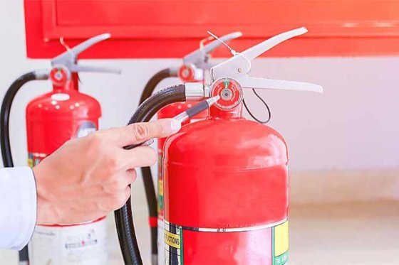 A hand releasing the safety pin on a rack of red fire extinguishers